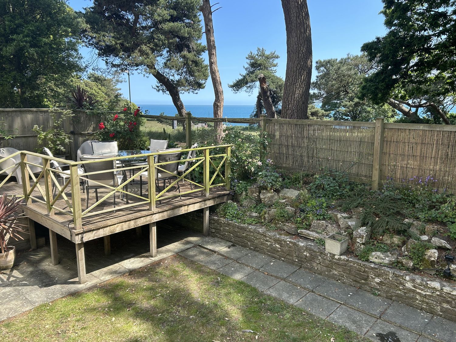 A garden with a deck, table, and chairs overlooking the sea at Hoppapill House in Bournemouth