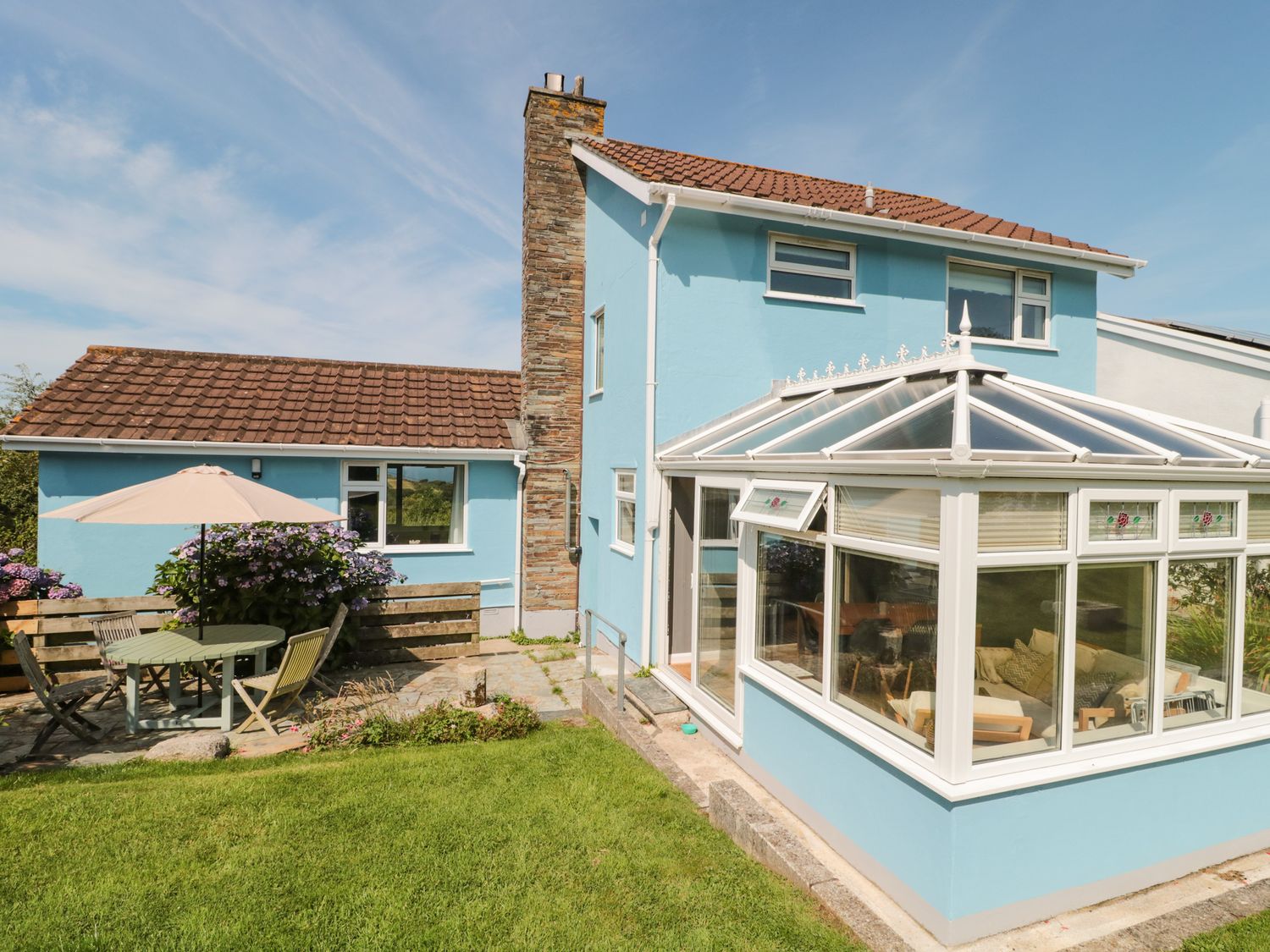 A blue two story house with a conservatory and a patio with table and chairs at Honeycroft in Boscastle