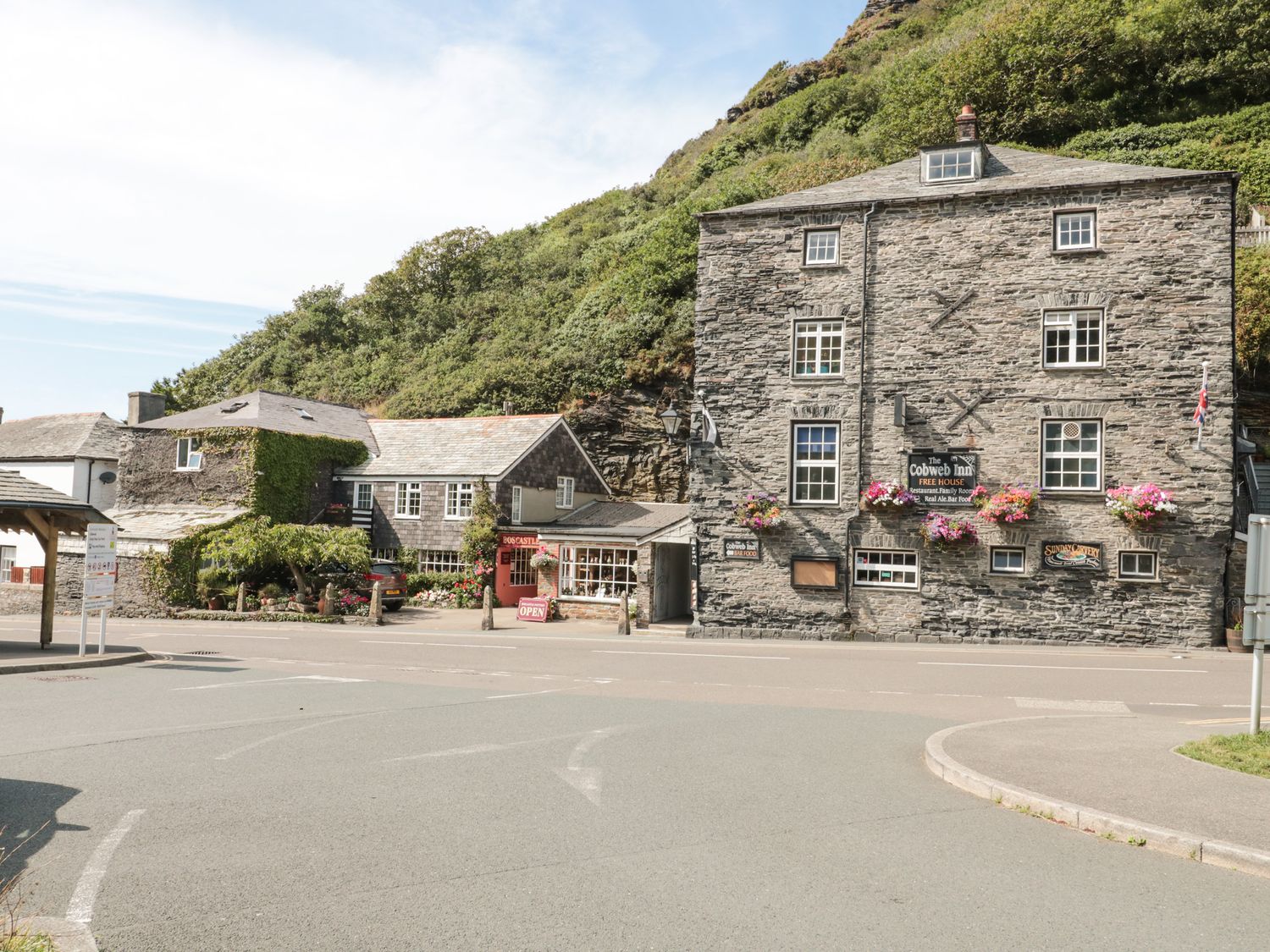 A street view of stone buildings with flower baskets and a sign for The Cobweb Inn at Honeycroft in Boscastle
