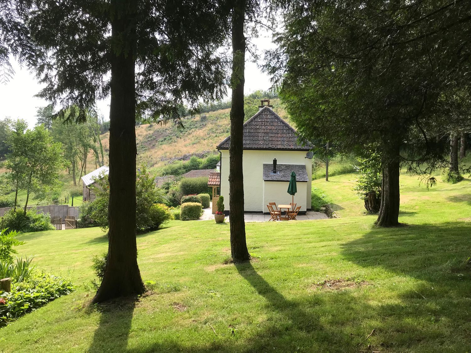 A garden with trees and a small patio with a table and chairs outside a cottage at Barn Owl Cottage in Wheddon Cross
