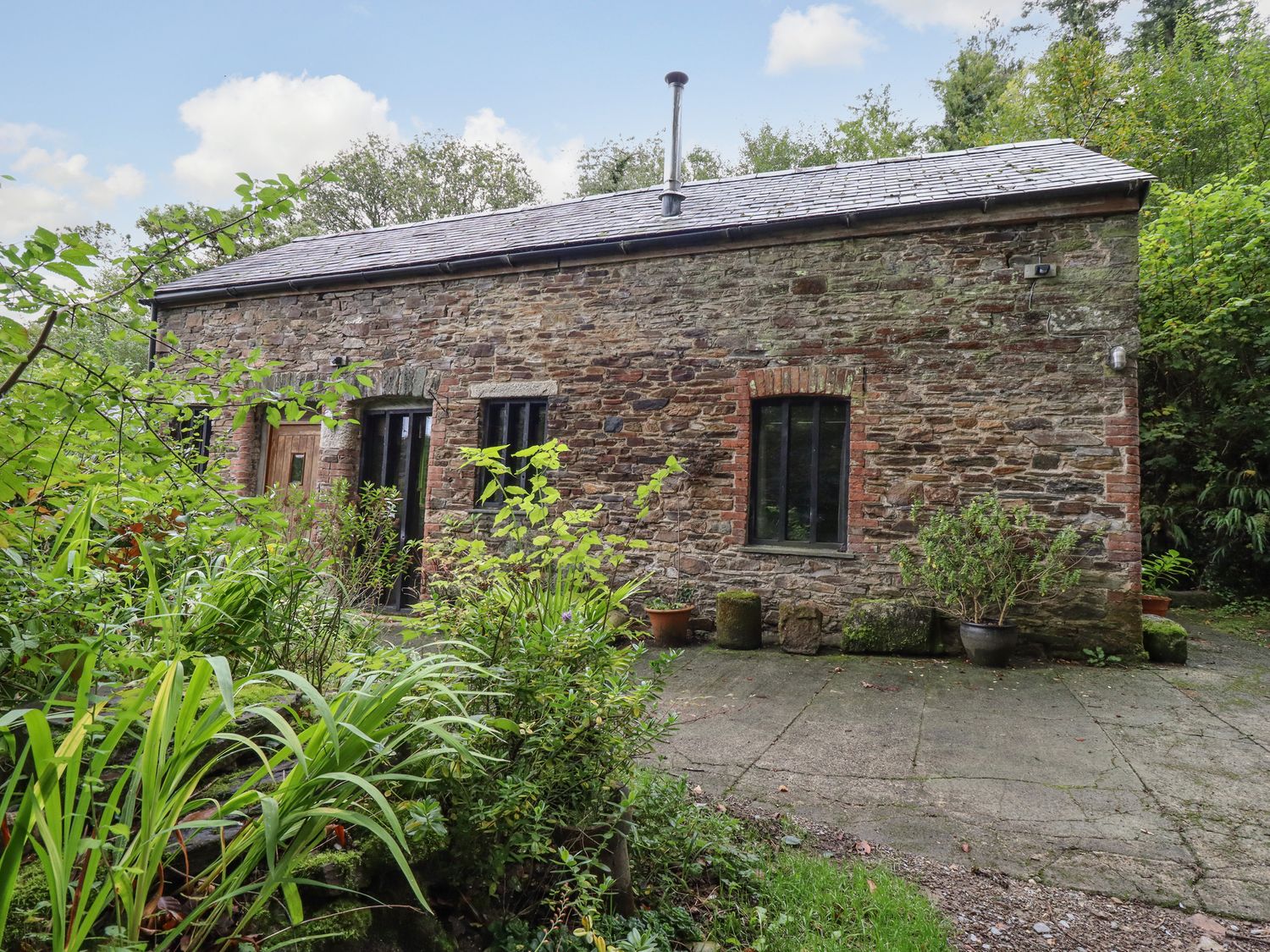 A stone house with a slate roof surrounded by plants and trees at Tamar Barn in Gulworthy