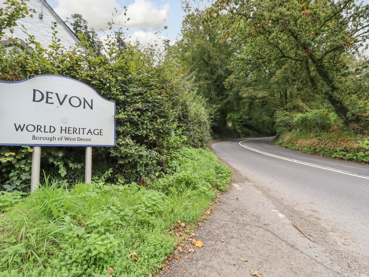 A curved road with trees on both sides and a Devon world heritage sign at Tamar Barn in Gulworthy