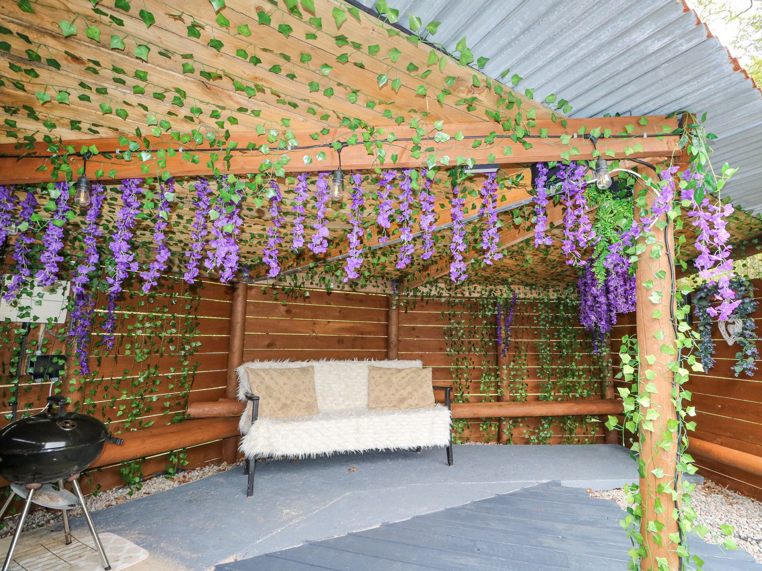 A covered outdoor seating area with a bench and hanging plants at Grant Cottage in Strontian