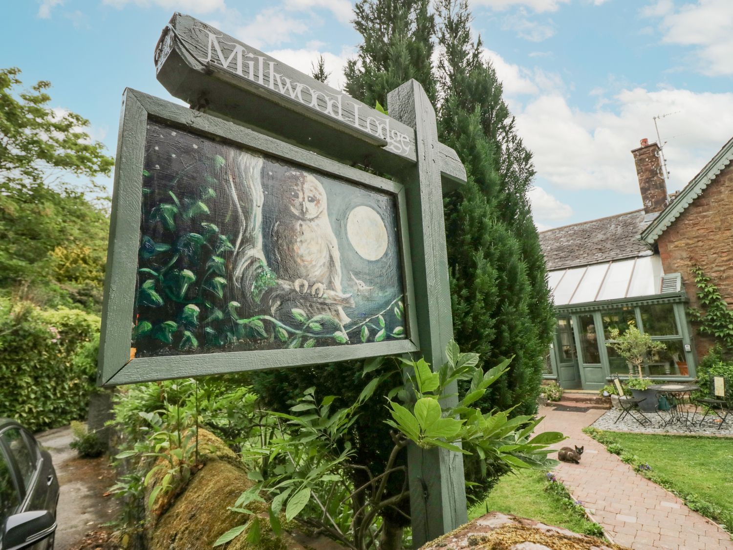 A wooden sign with an owl painting in a garden near a stone house at Millwood Lodge in Barrow-In-Furness