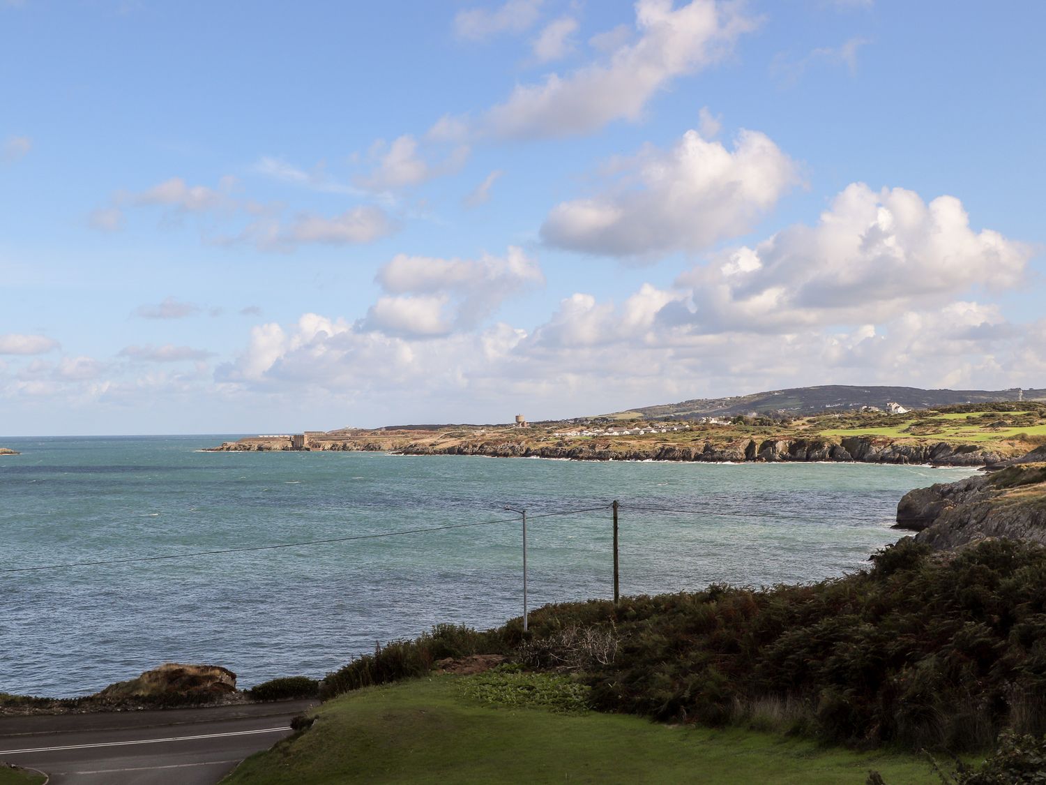A coastal landscape with a road, grass, and bushes by the sea at Ser a Mor Stars and Sea Bull Bay near Amlwch