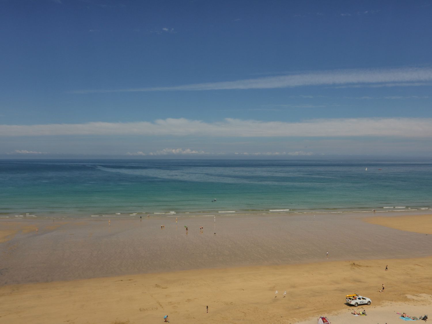 A beach with people on the sand and in shallow water and a rescue vehicle on the shore at 13 Cliff Edge in Newquay