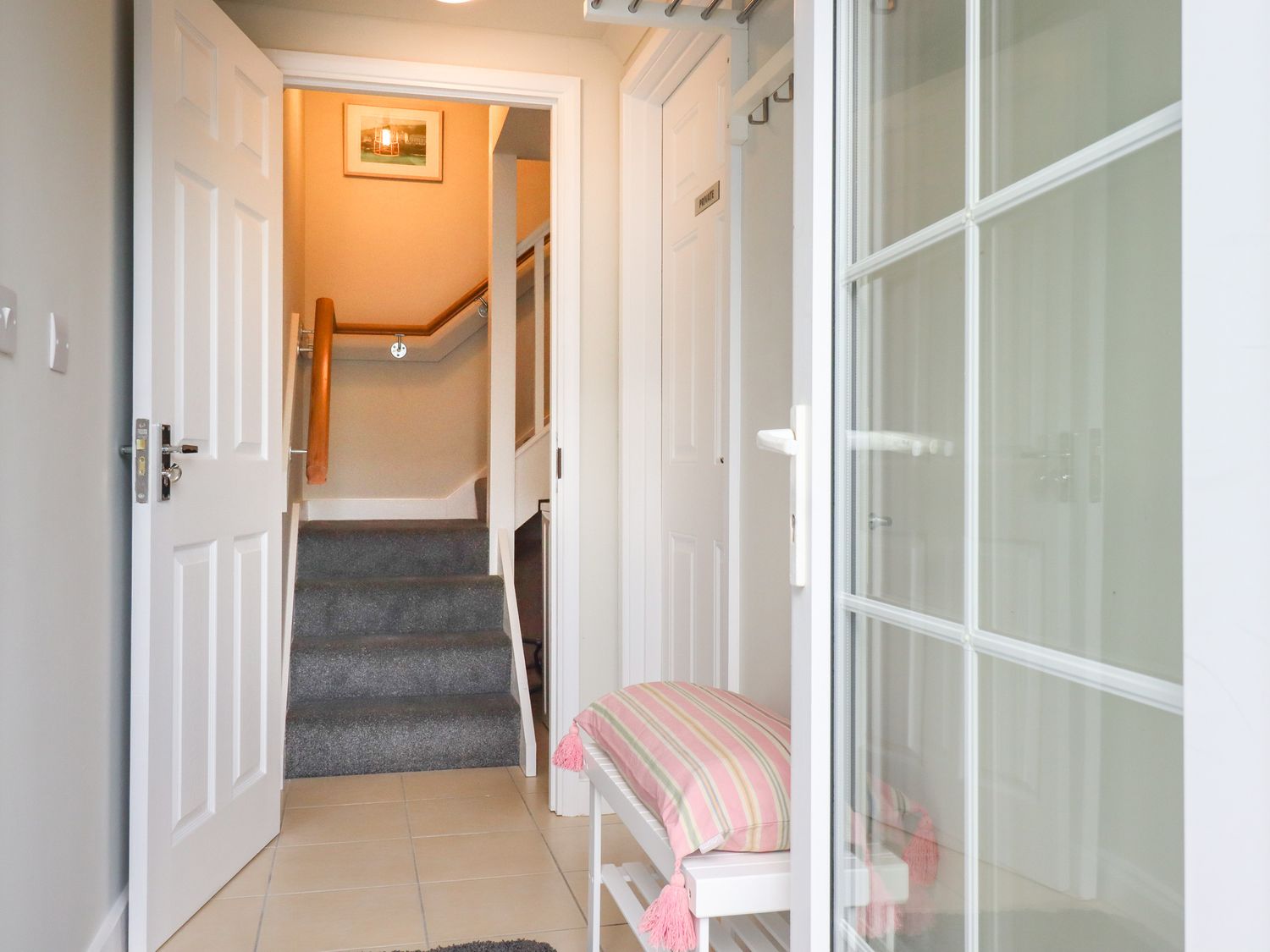 A hallway with tiled floor a staircase with carpet a bench with a striped cushion and a door marked private at Poppy Lodge in Bolingey near Perranporth