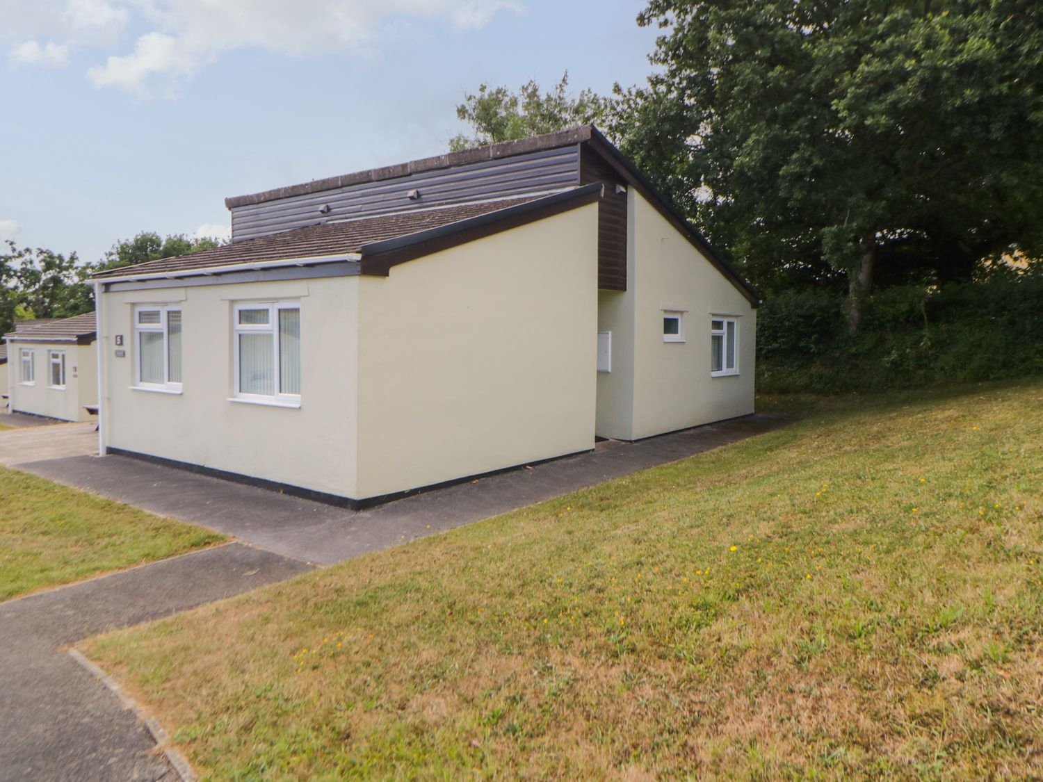 A bungalow with cream walls and white windows on a grassy slope at Harcombe House  Bungalow 5 in Chudleigh