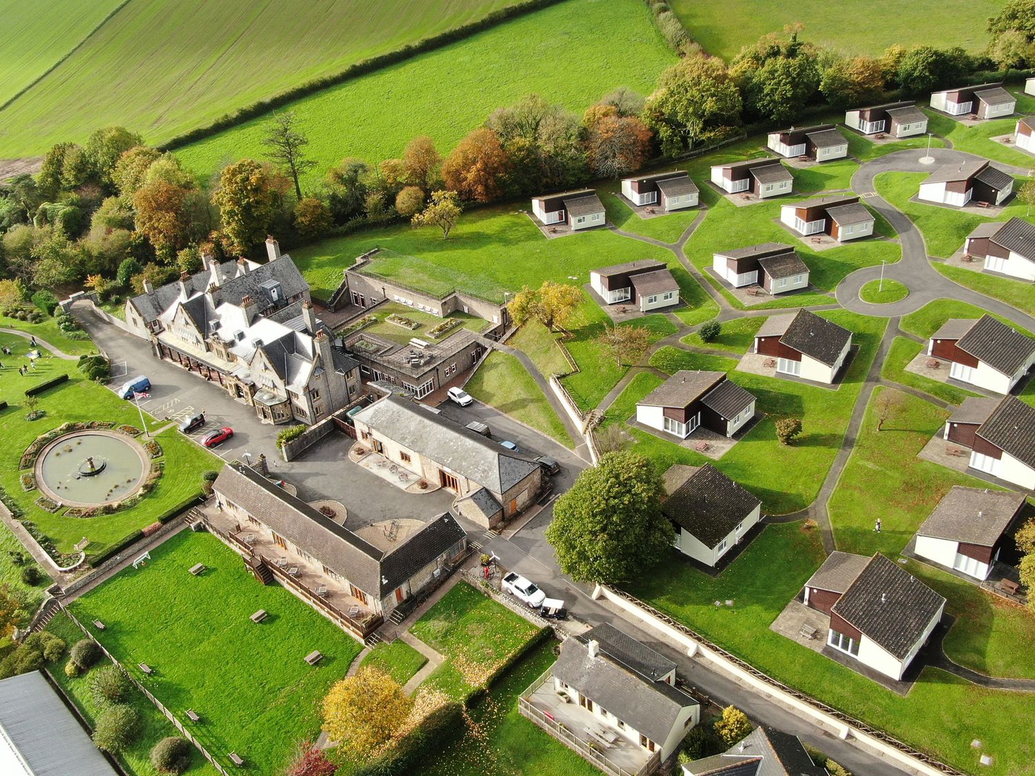 An aerial view of a residential area with multiple small houses roads and a large building surrounded by green fields and trees at Harcombe House Bungalow 10 in Chudleigh