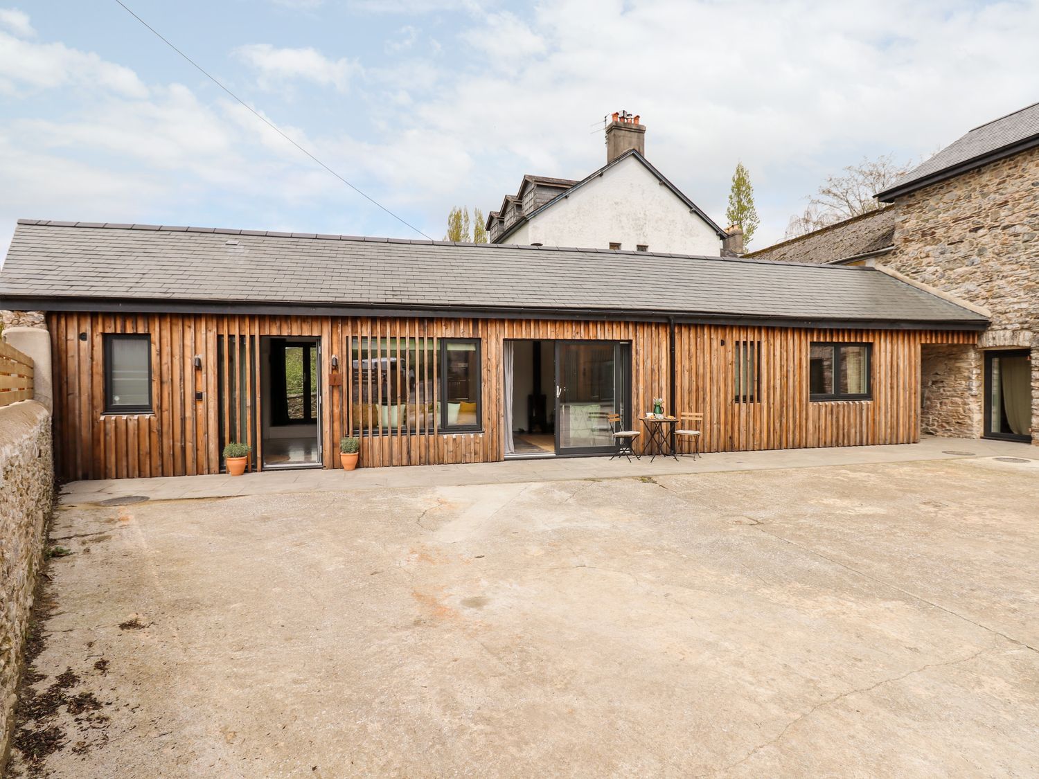 A wooden barn style house with stone walls and a concrete courtyard at 1 Caddaford Barns in Buckfastleigh