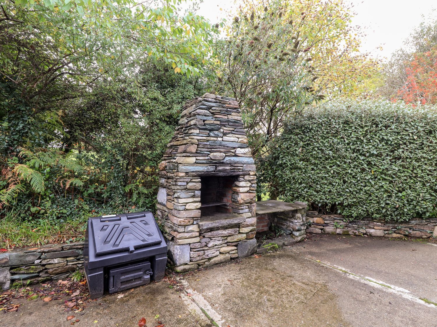 An outdoor stone barbecue grill next to a black storage box surrounded by green bushes at Seascape Lodge Kenmare County Kerry