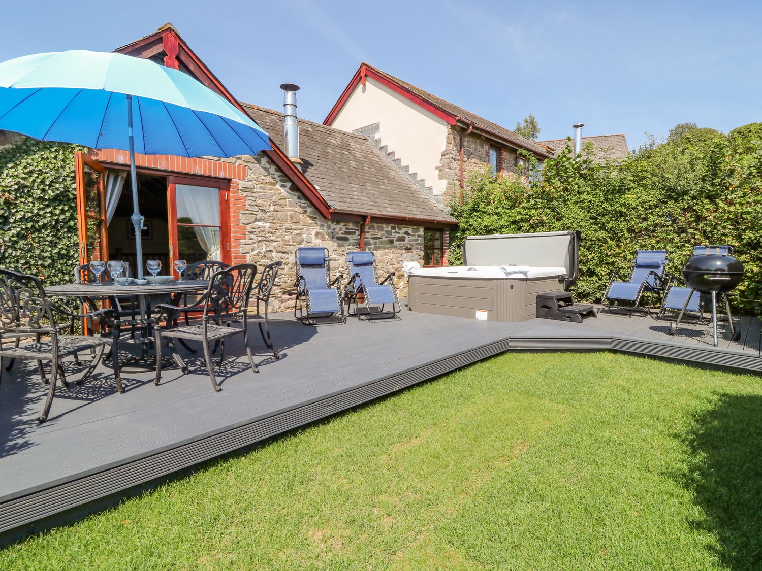 An outdoor patio with a dining table and umbrella lounge chairs hot tub and barbecue grill at Oak Cottage in North Molton