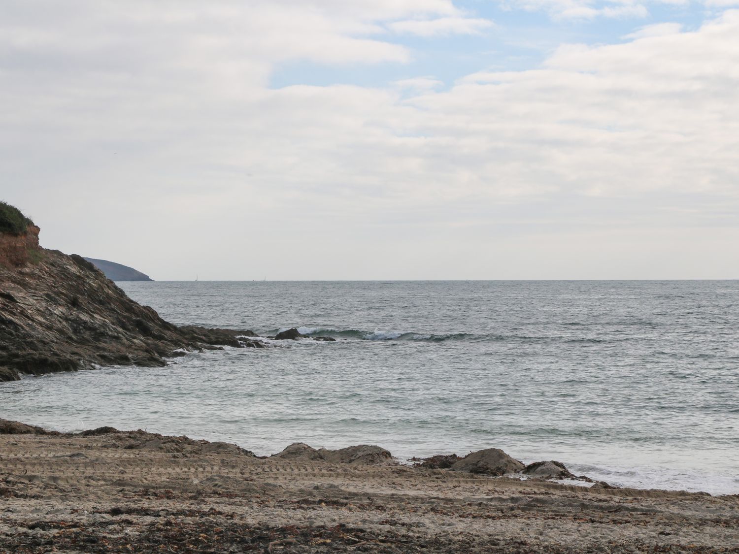 A rocky beach with tire tracks near the shore and the ocean under a cloudy sky at Riverside Summercourt in Penryn