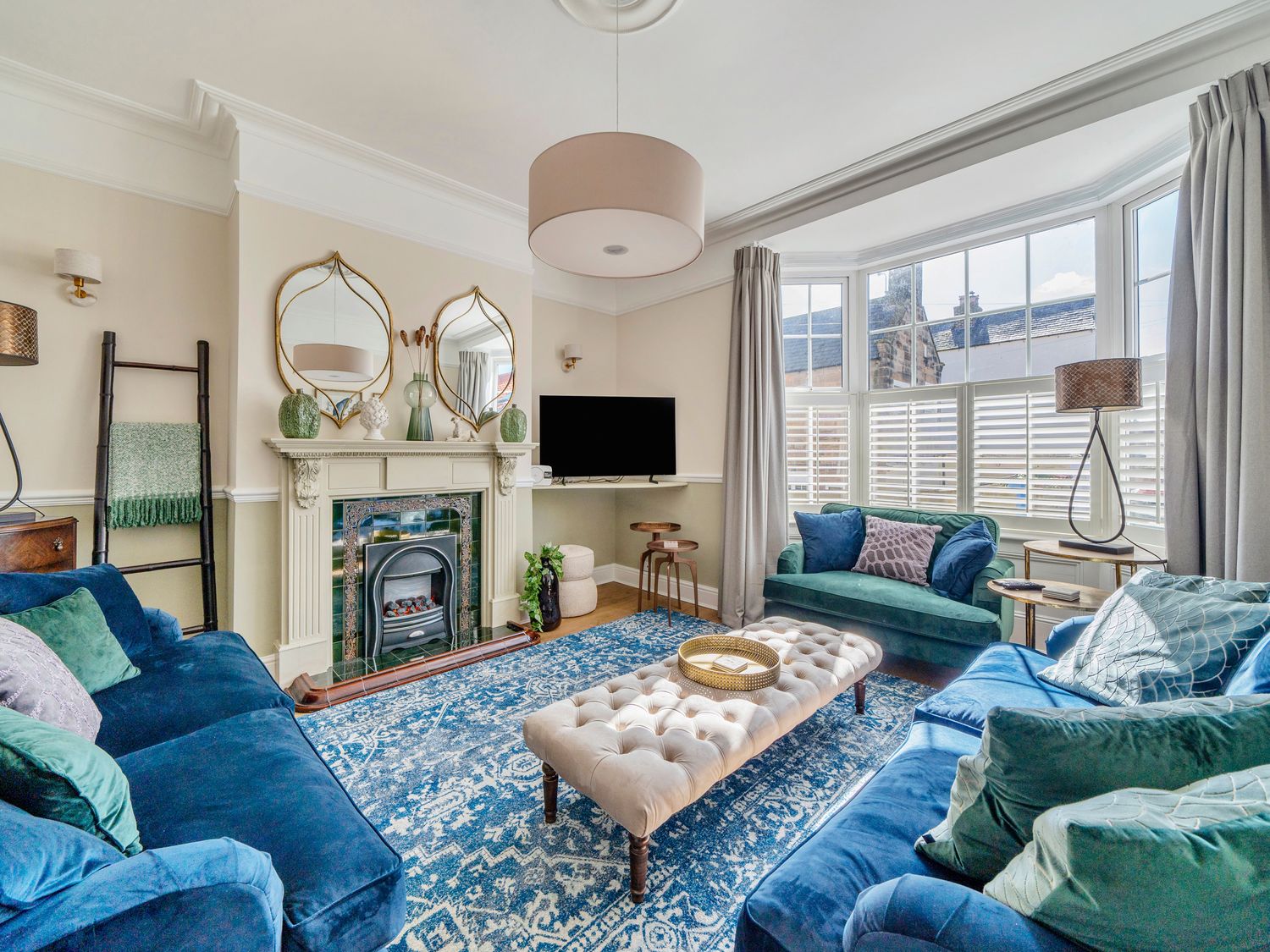 A living room with blue and green sofas a fireplace and a large window at Regatta House in Whitby