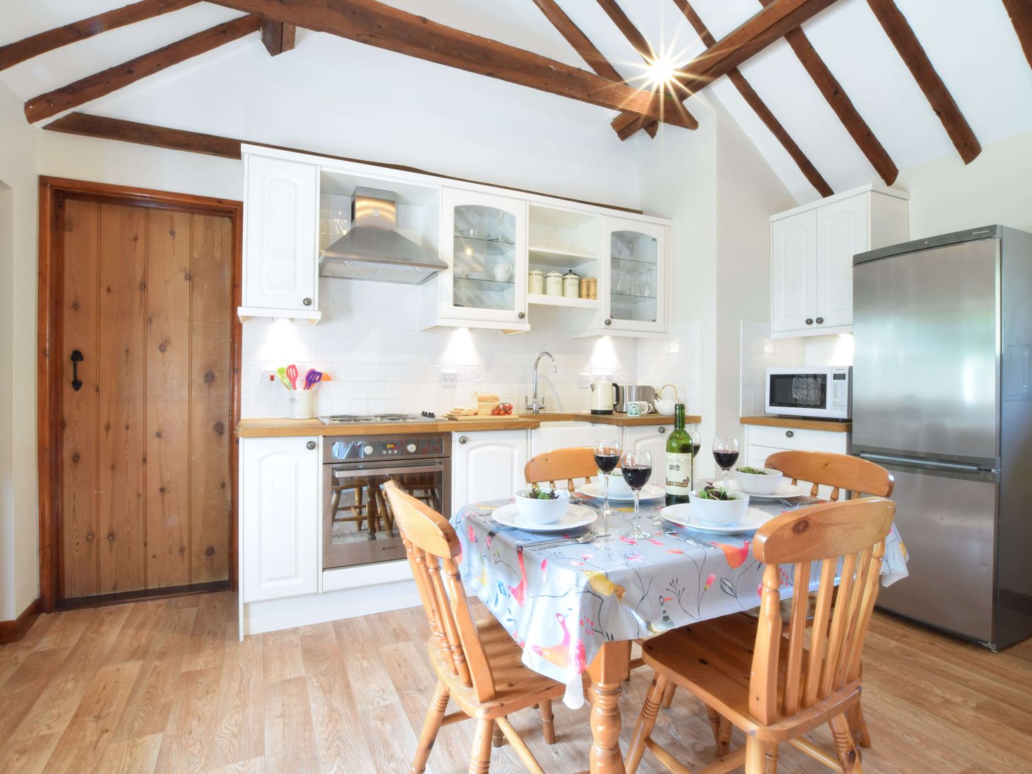 A kitchen with wooden dining table and chairs a stainless steel refrigerator and white cabinets at The Stables in Polstead