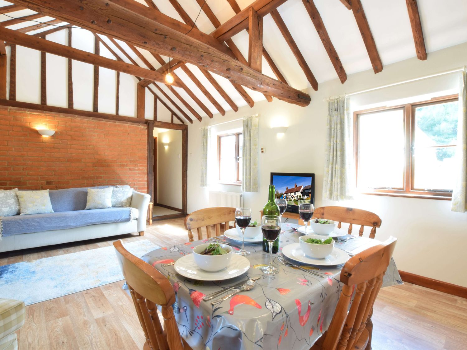 A dining table set with bowls and wine glasses in a room with exposed wooden beams and a sofa at The Stables in Polstead