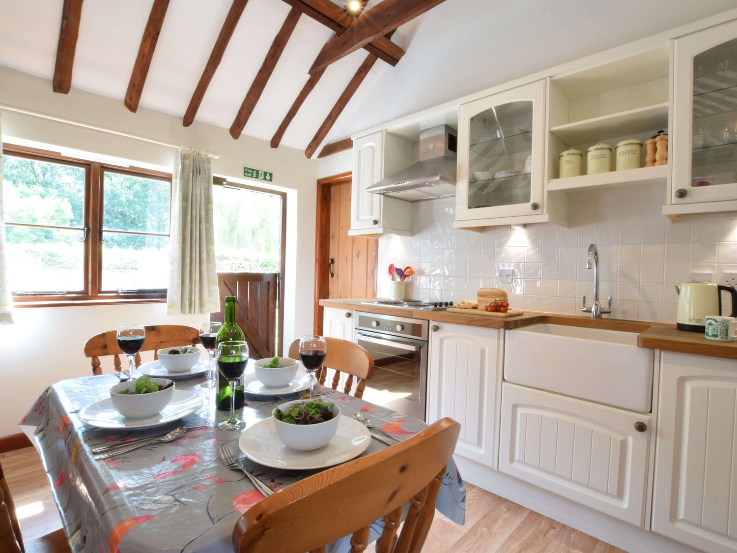 A kitchen with a dining table set for four with bowls of salad and glasses of red wine at The Stables in Polstead