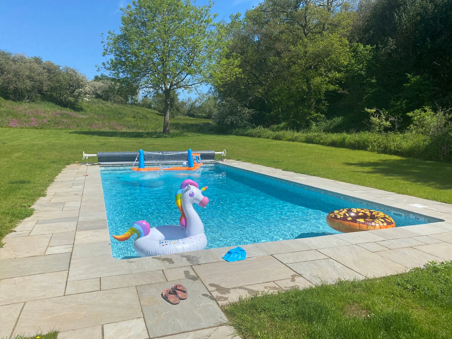 An outdoor swimming pool with inflatable toys and sandals on the stone poolside at The Stables in Polstead