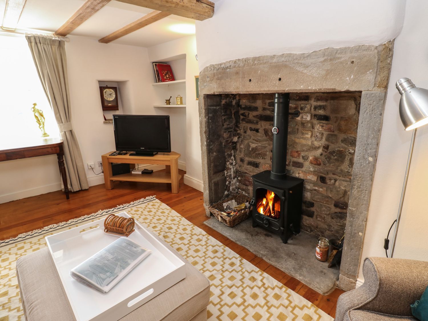 A living room with a stone fireplace and wood stove a tv on a wooden stand and a white tray on an ottoman at Cross View Cottage in Alston