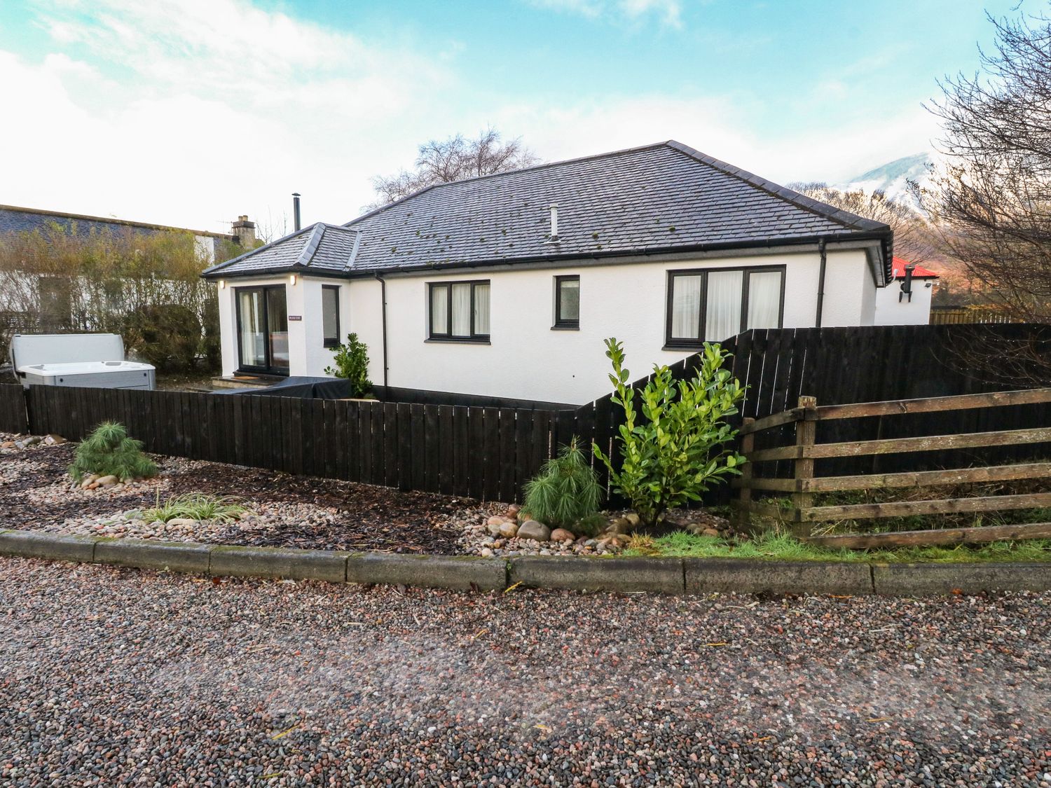 A single story house with white walls and grey roof surrounded by wooden fence and gravel driveway at Island View House in Glencoe