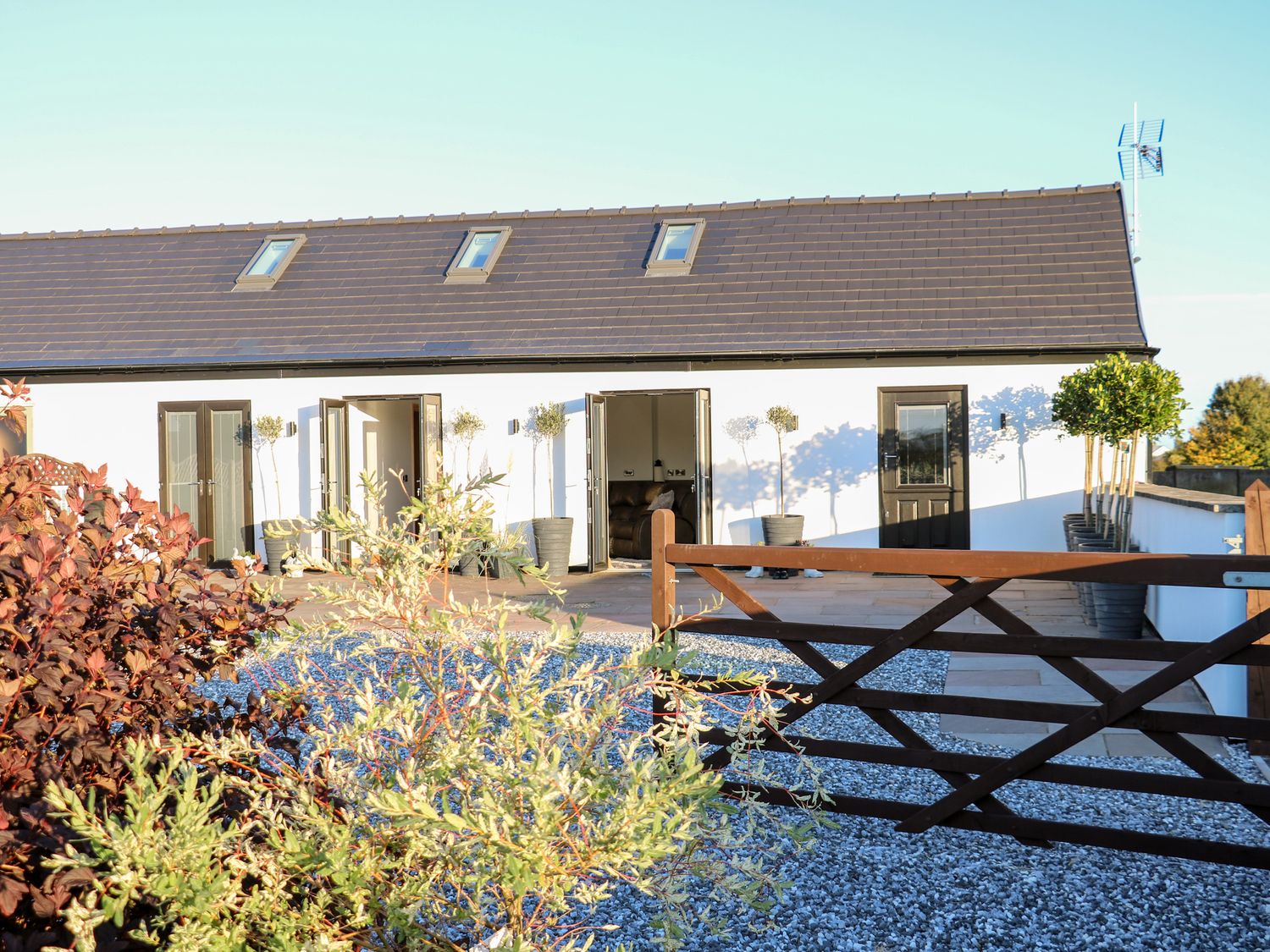 A white building with a brown gate and potted plants in front at Bear Cottage in Heage