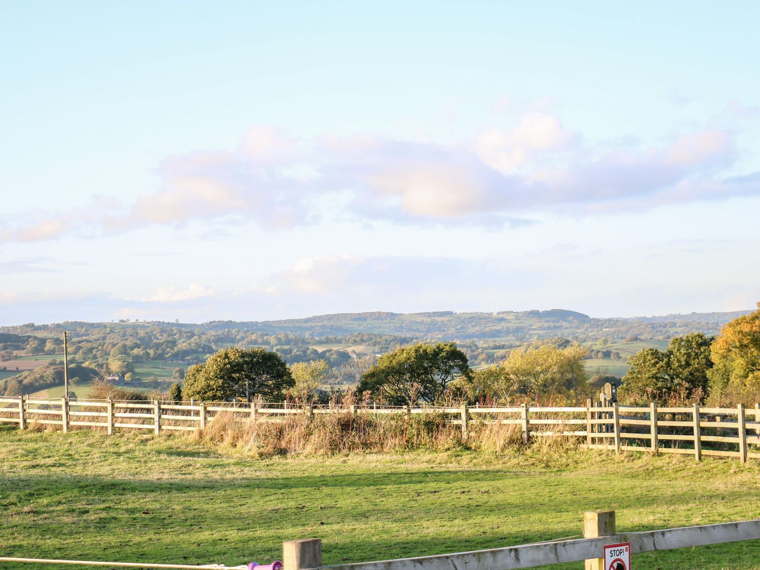 A fenced grassy field with trees and hills in the background at Bear Cottage in Heage