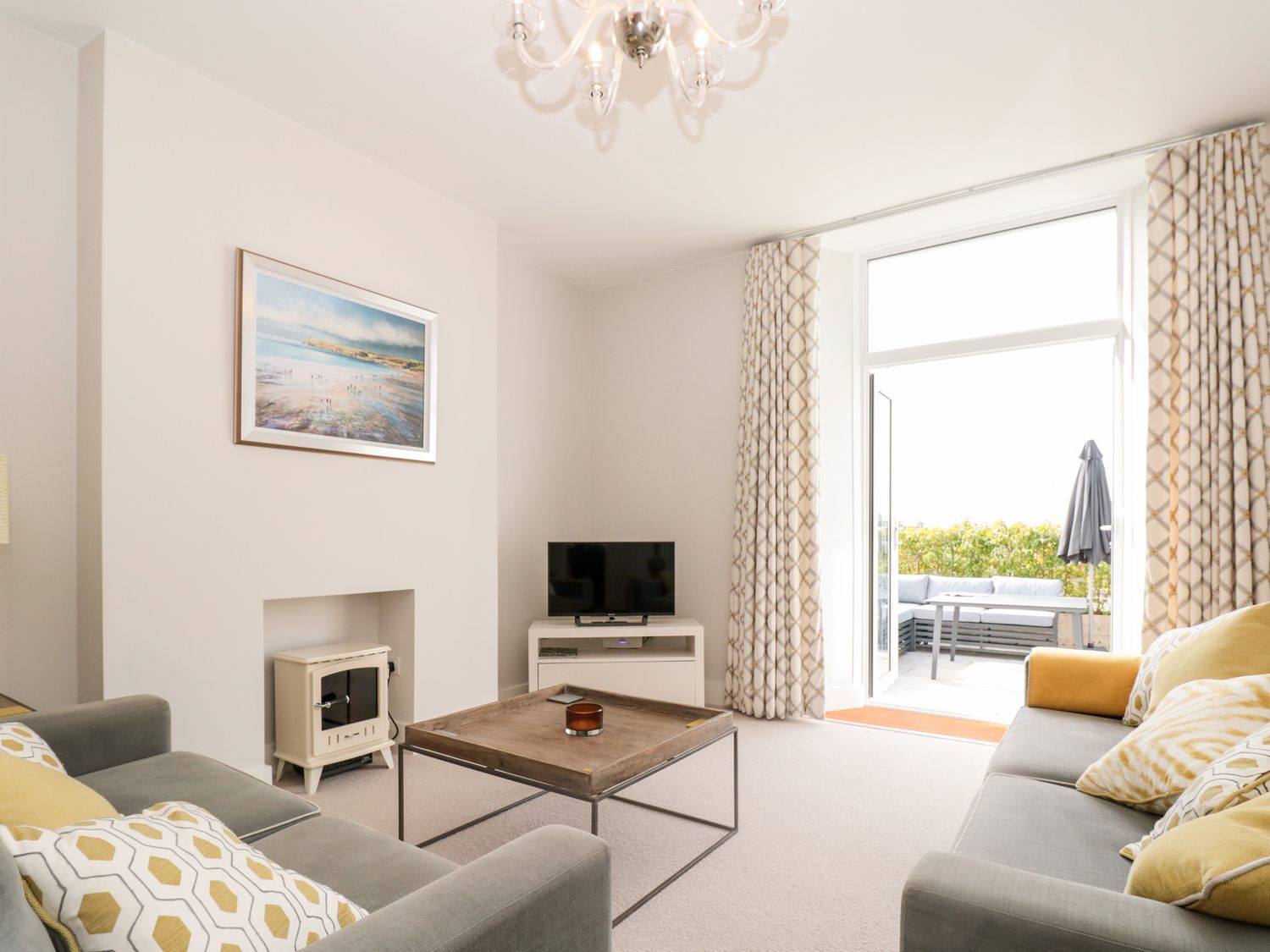 A living room with two sofas a wooden coffee table a small stove a television and glass doors leading to an outdoor seating area at 2 The Manor House Hillfield Village in Dartmouth