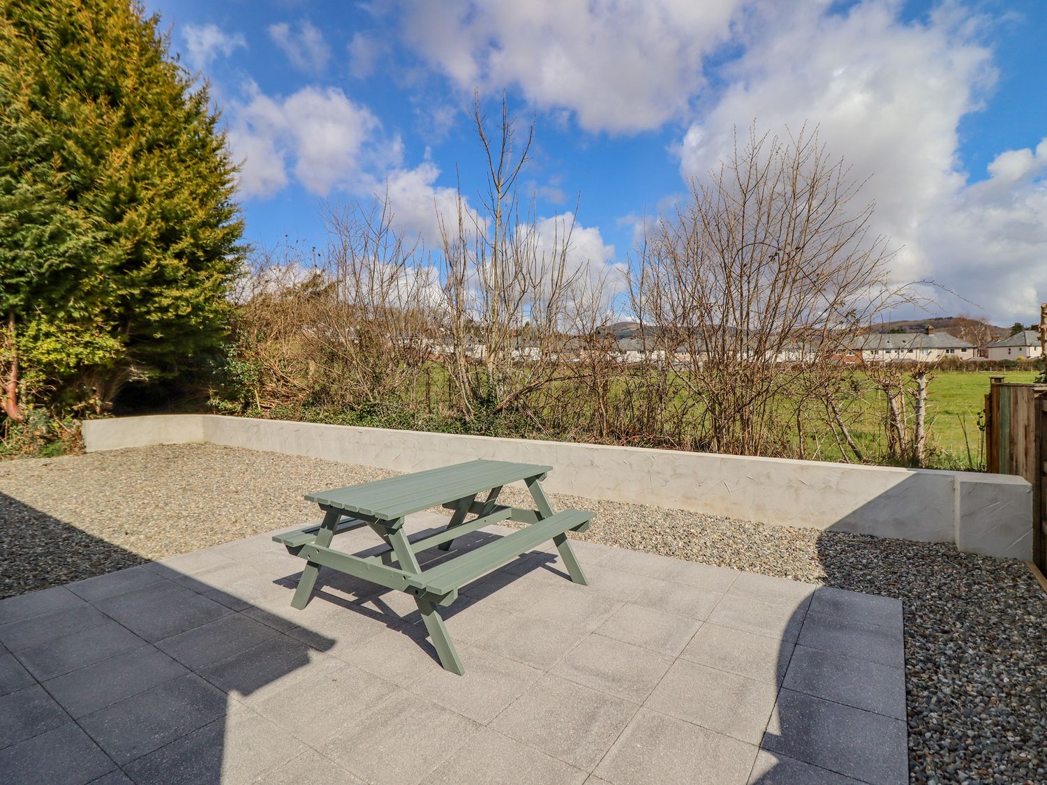 A patio with a green picnic table and gravel area next to a grass field at Mawnog Fach in Bala