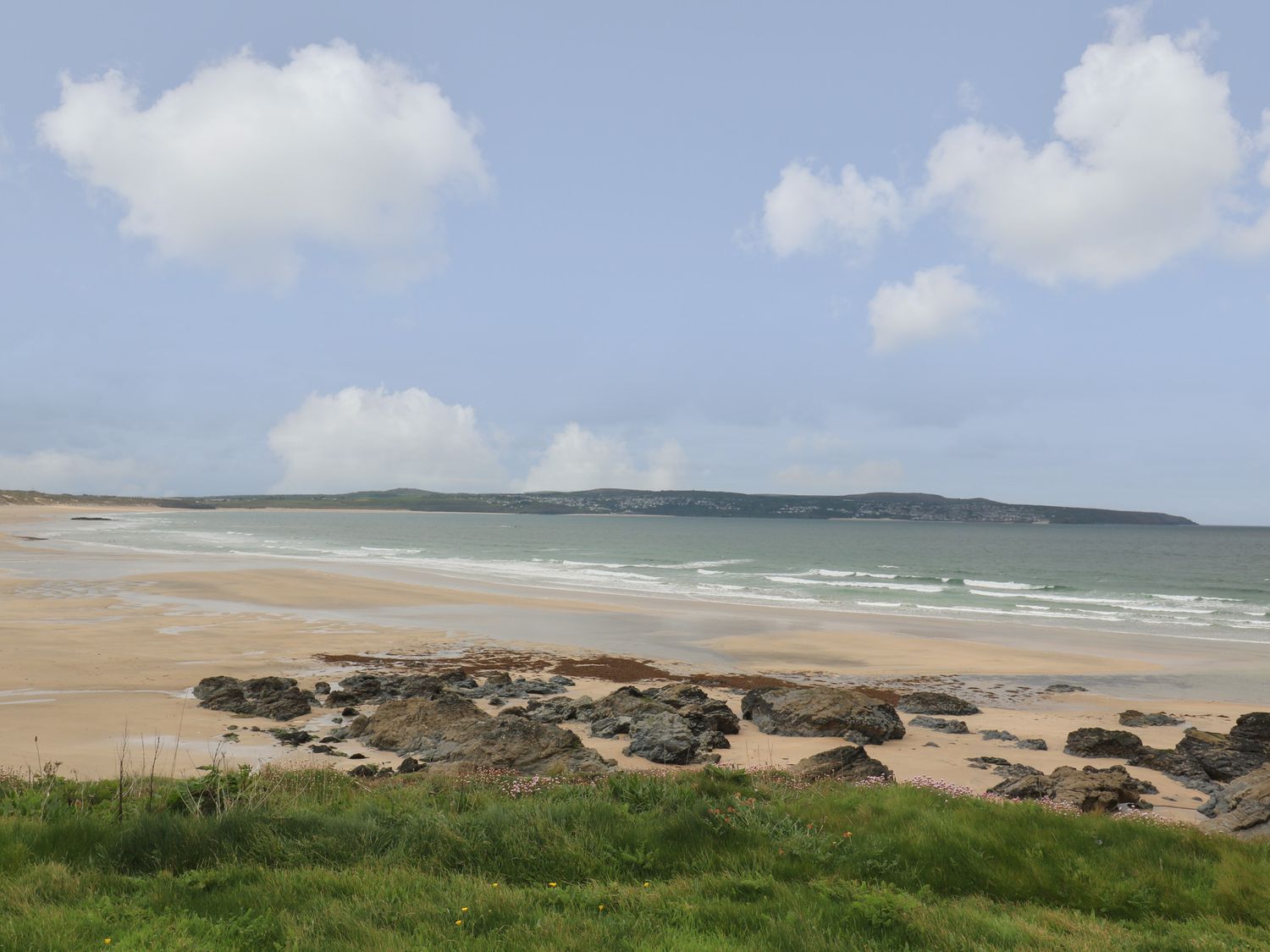 A sandy beach with rocks and grass near the shore and hills in the background at Tredarn in Connor Downs