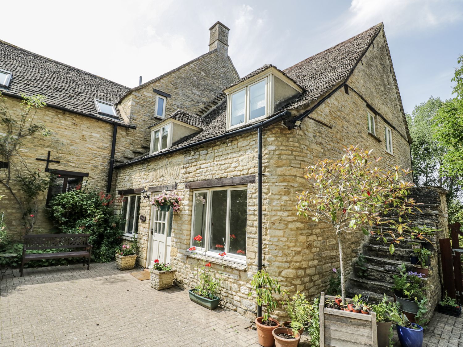 A stone building with a door and windows and a garden area at Dairy Cottage in Witney