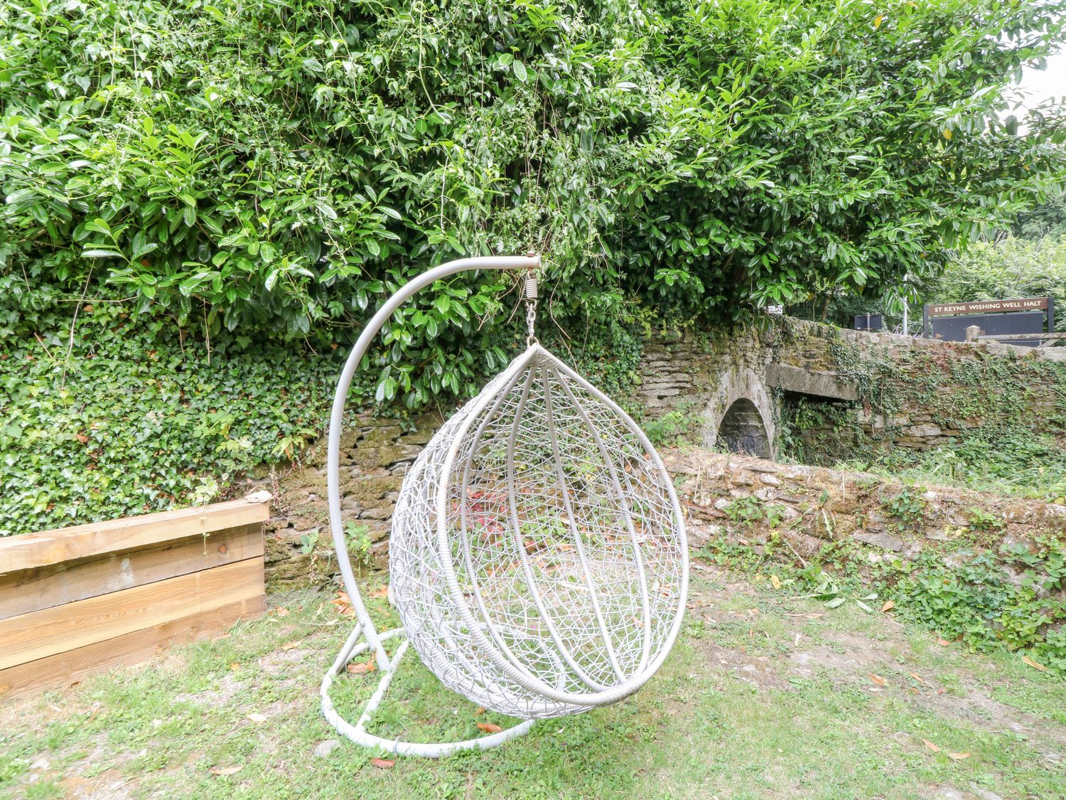 A hanging garden chair in a yard with ivy and stone walls at Millers Lodge in St Keyne near Liskeard