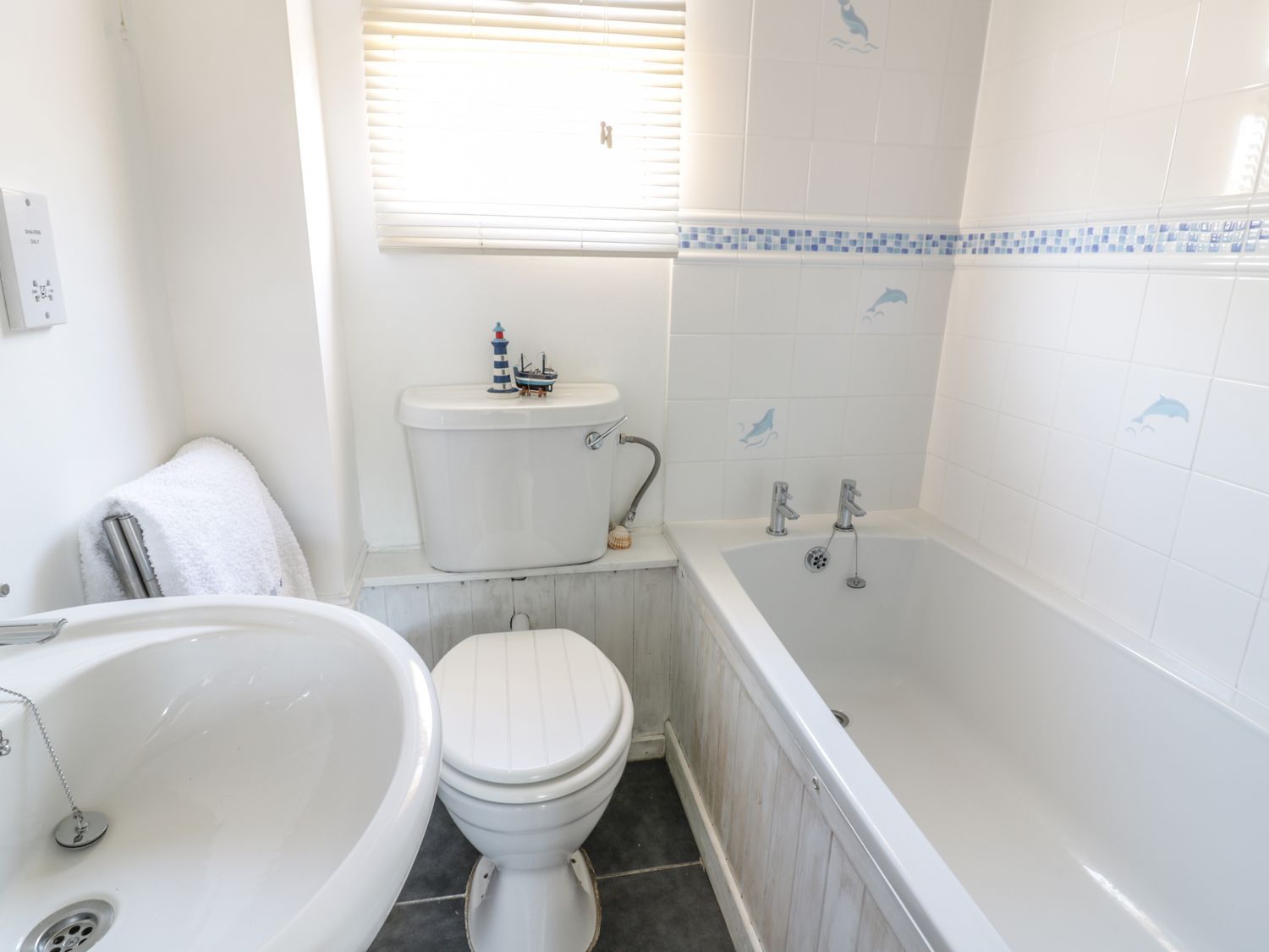 A bathroom with a sink a toilet and a bathtub with dolphin tiles at Chalet 216- The Beach Retreat Atlantic Bays Holiday Park near St Merryn