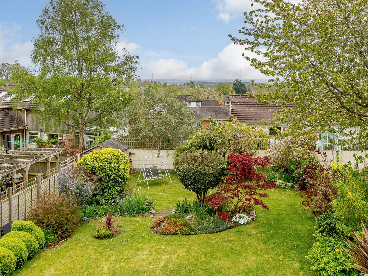 A residential garden with green grass trees shrubs and a garden swing at Caradoc Tutshill near Chepstow