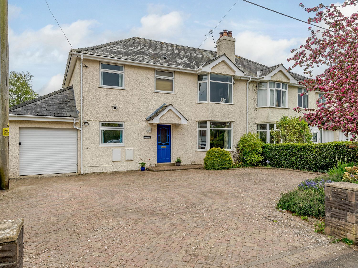 A semi detached house with a blue door a garage and a driveway with bushes and a tree at Caradoc Tutshill near Chepstow