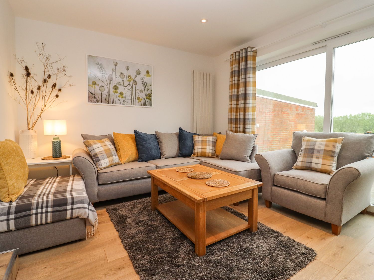 A living room with gray sofas yellow and plaid cushions a wooden coffee table and a large window at Delabere Road in Bishops Cleeve