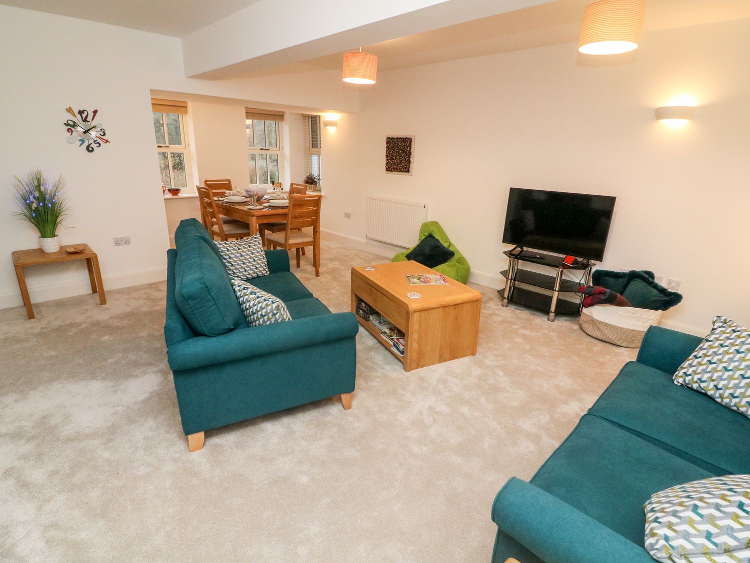 A living room with teal sofas a wooden coffee table a television and a dining area at Bronte House Kirkby Lonsdale