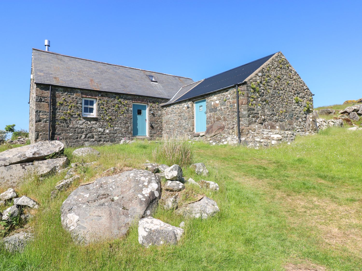 A stone cottage with blue doors and a grassy area with rocks at Ty Mellen in Dinas Cross