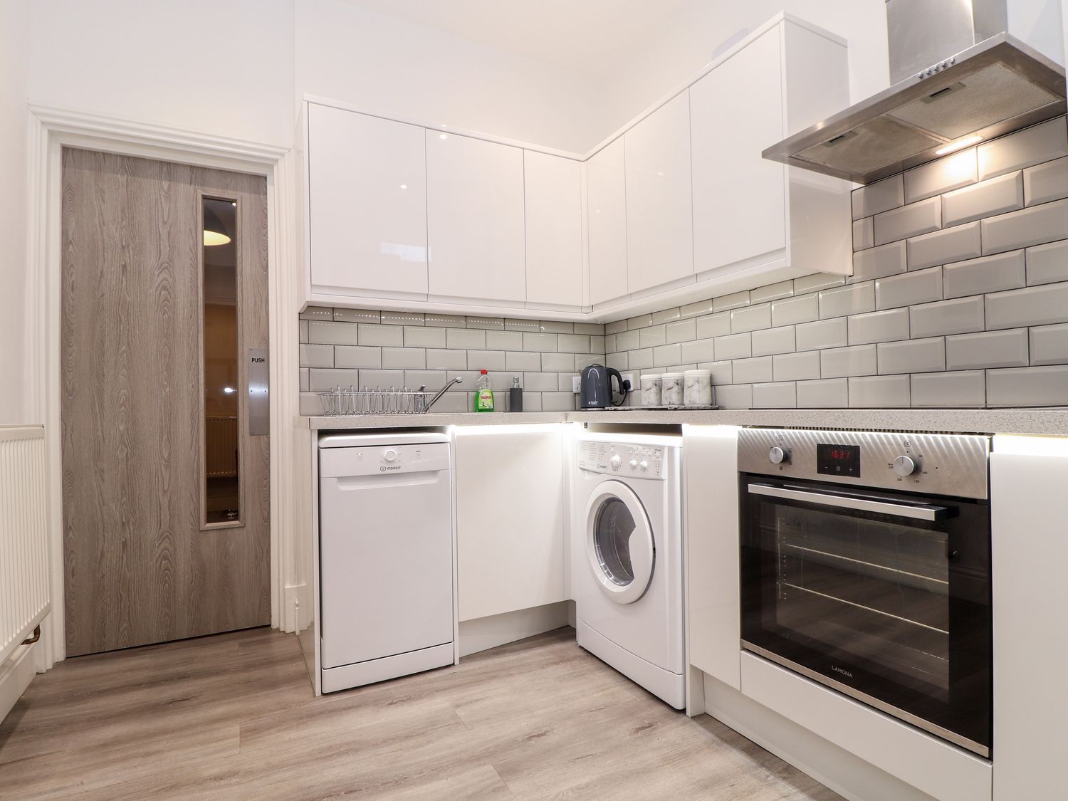 A kitchen with white cabinets dishwasher washing machine oven and a wooden door at Teylu in Camborne