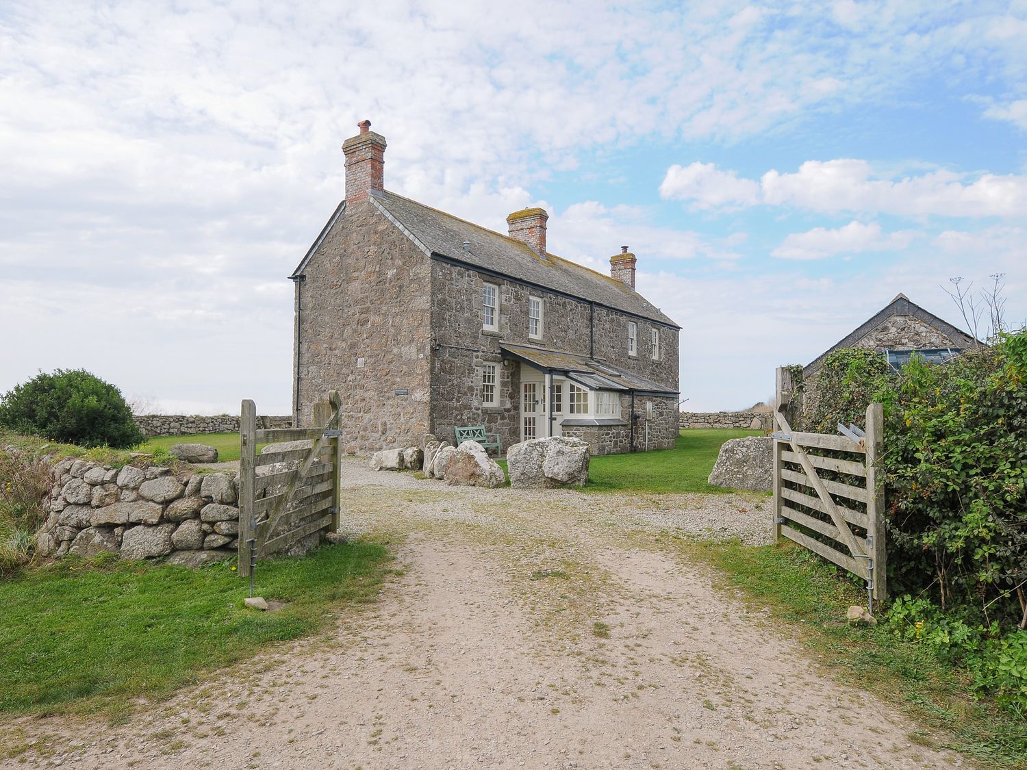 A stone house with chimneys and a gravel driveway with open wooden gates at Three Chimneys St Levan near Porthgwarra