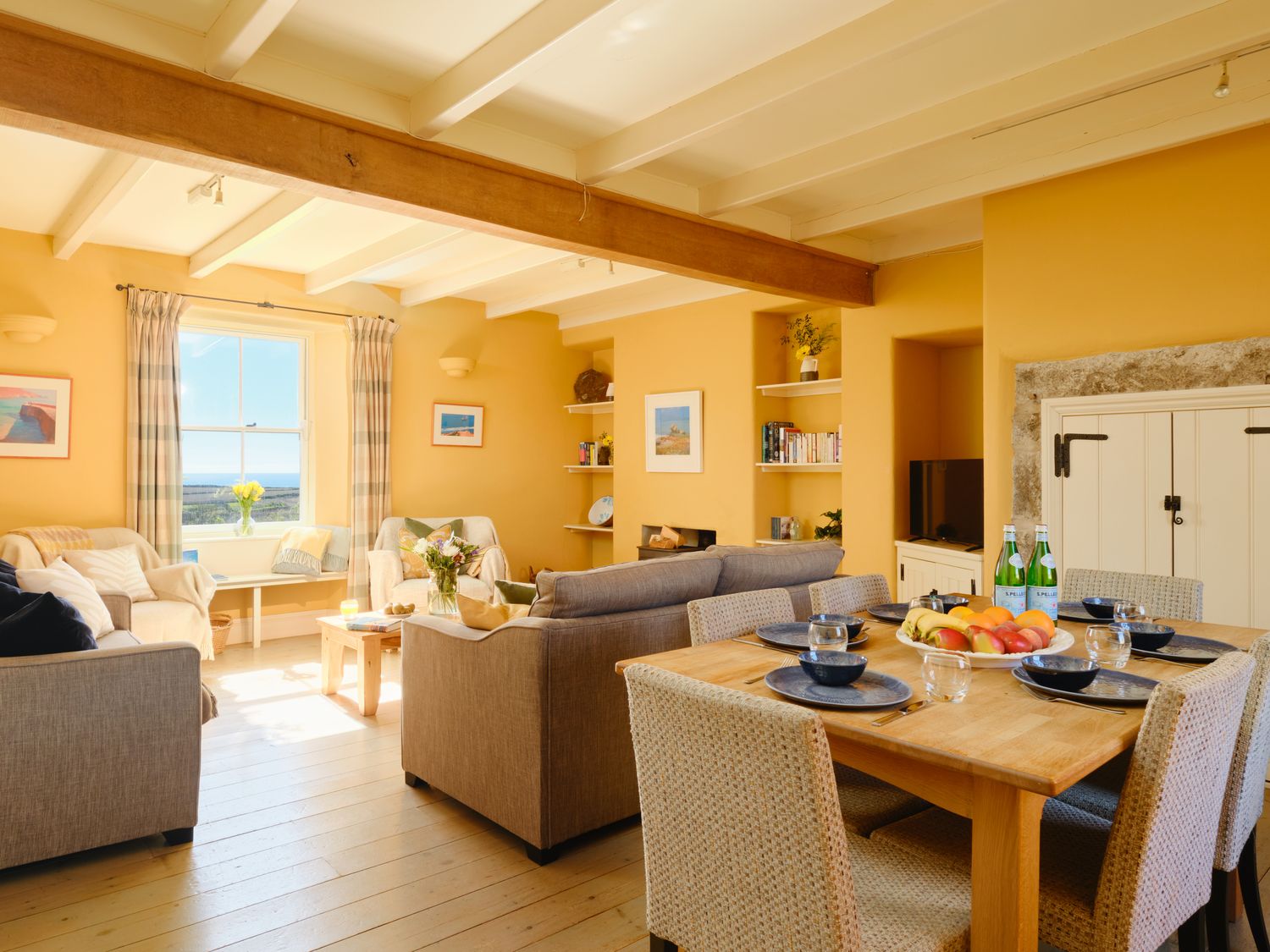A living room with sofas a coffee table a dining table set with plates and glasses and a window with curtains at Higher Roskestal St Levan near Porthgwarra