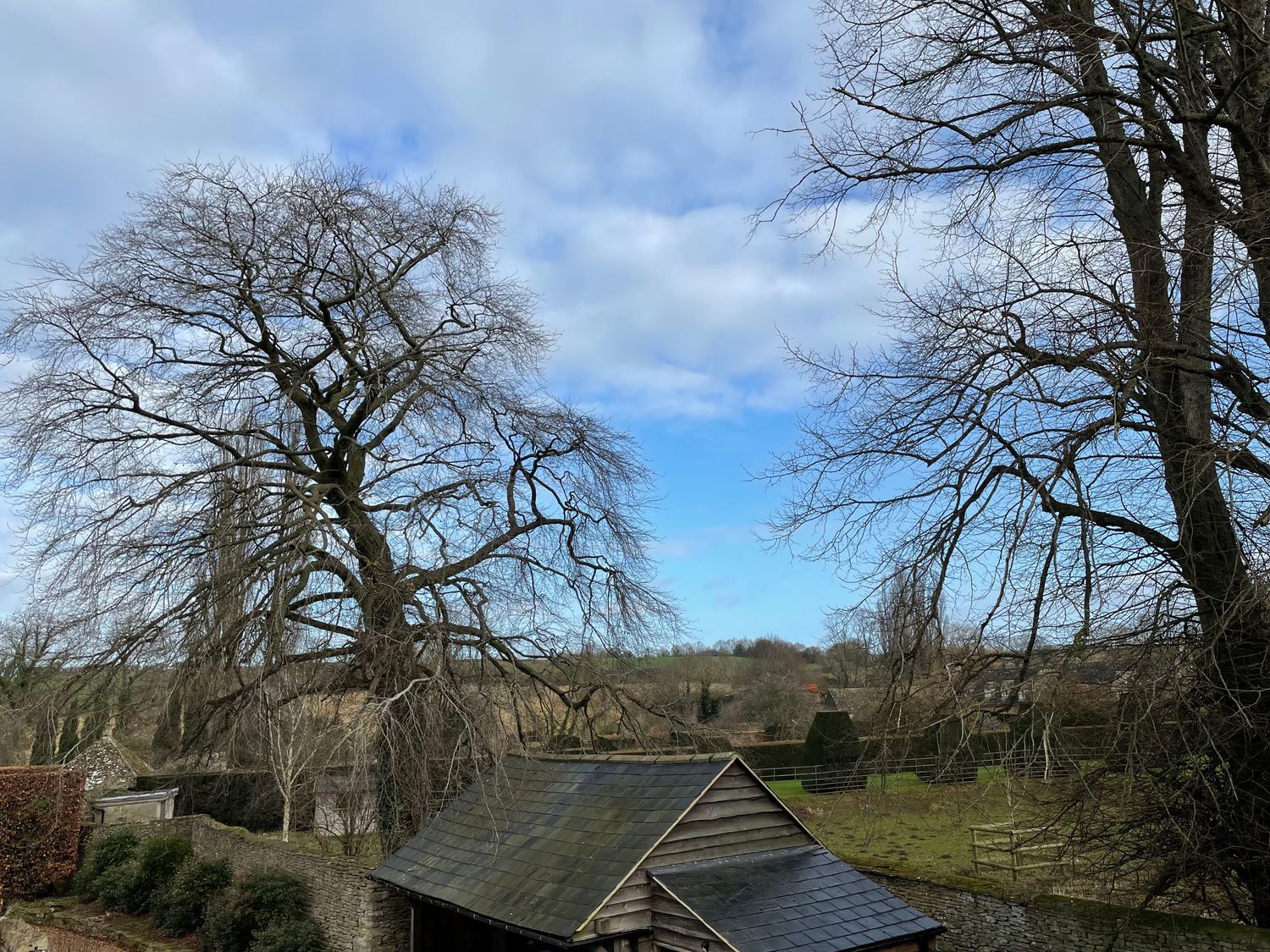 A rural landscape with leafless trees a small wooden shed a stone wall and open fields at Omas Cottage in Moreton-In-Marsh