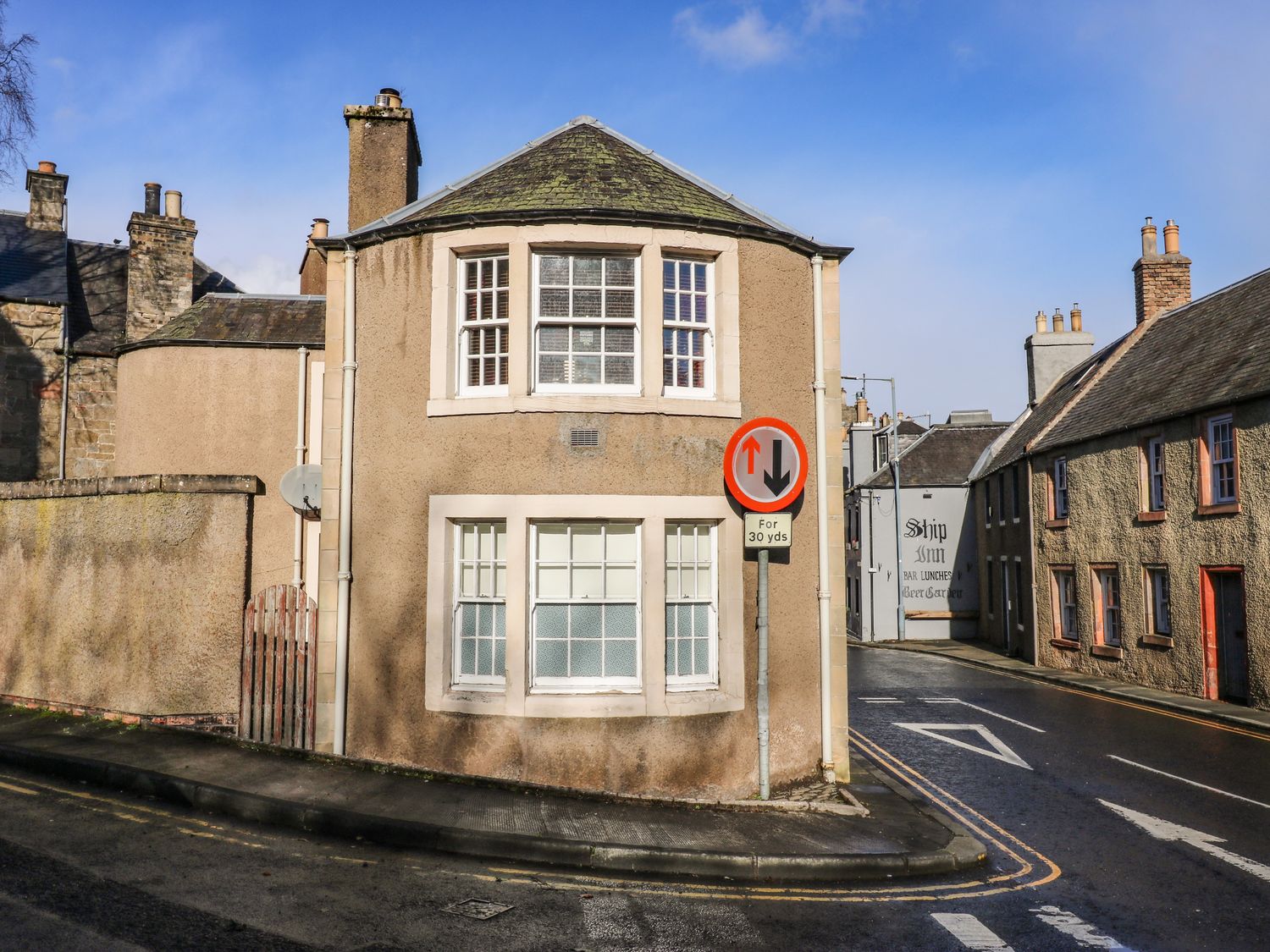 A street corner with beige buildings and a traffic sign showing priority for oncoming vehicles at The Toll House in Melrose