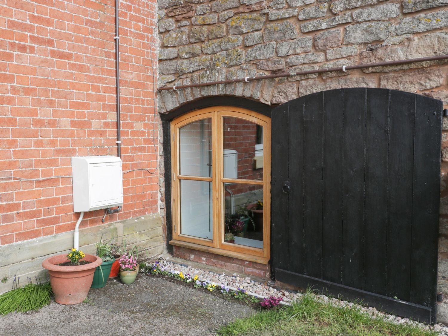 A window with wooden frame and black wooden door on a brick and stone wall with flower pots outside Lower Venn Granary Apartment 1 Sutton St Nicholas near Bodenham