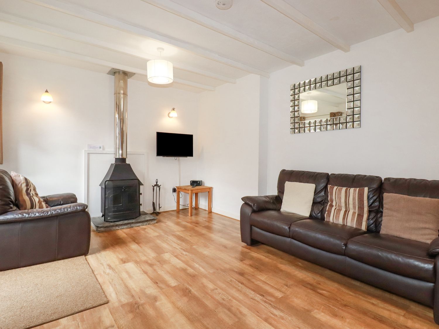 A living room with two leather sofas a fireplace a wall-mounted TV and a mirror at Bracken Cottage in St Tudy
