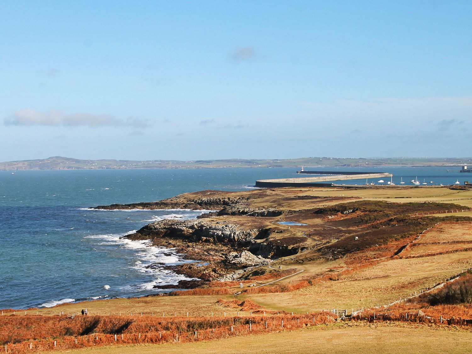 A coastal landscape with rocky shore and a pier with boats at Swn Y Nant in Holyhead