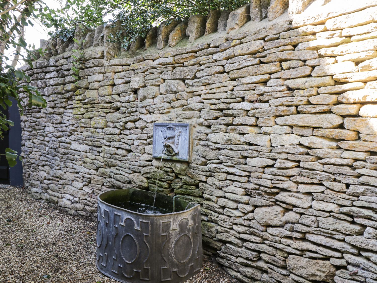 A stone wall with a decorative water fountain and metal basin in an outdoor garden at Rose Cottage in Corsham