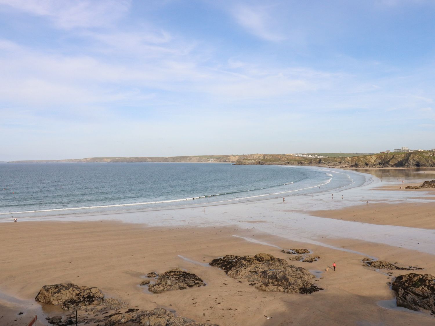 A sandy beach with rocks and people walking near the water at King Edward's View in Newquay