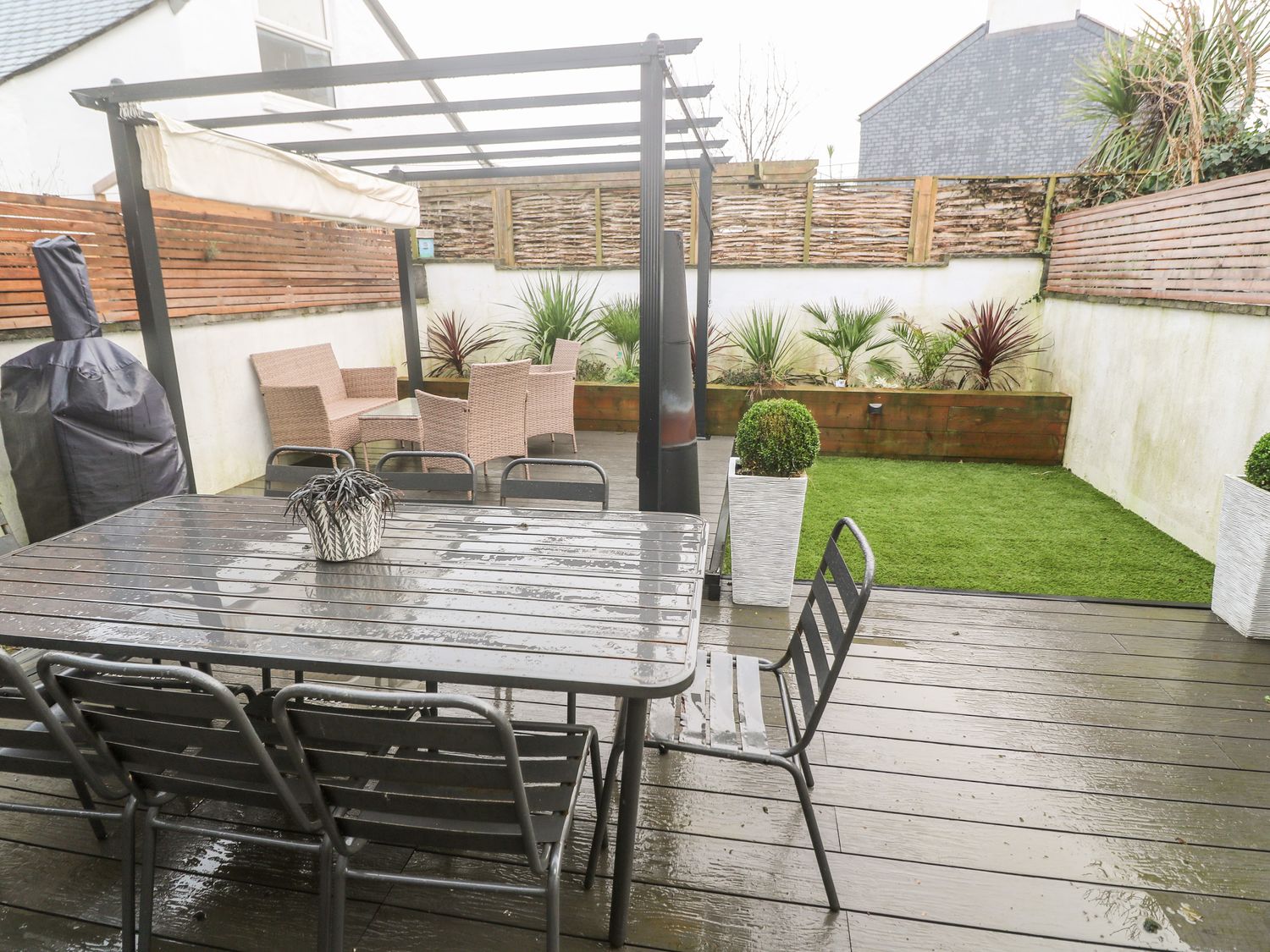 An outdoor patio with a metal dining table and chairs a covered seating area with wicker furniture and plants in pots at Tregenna House in St Ives