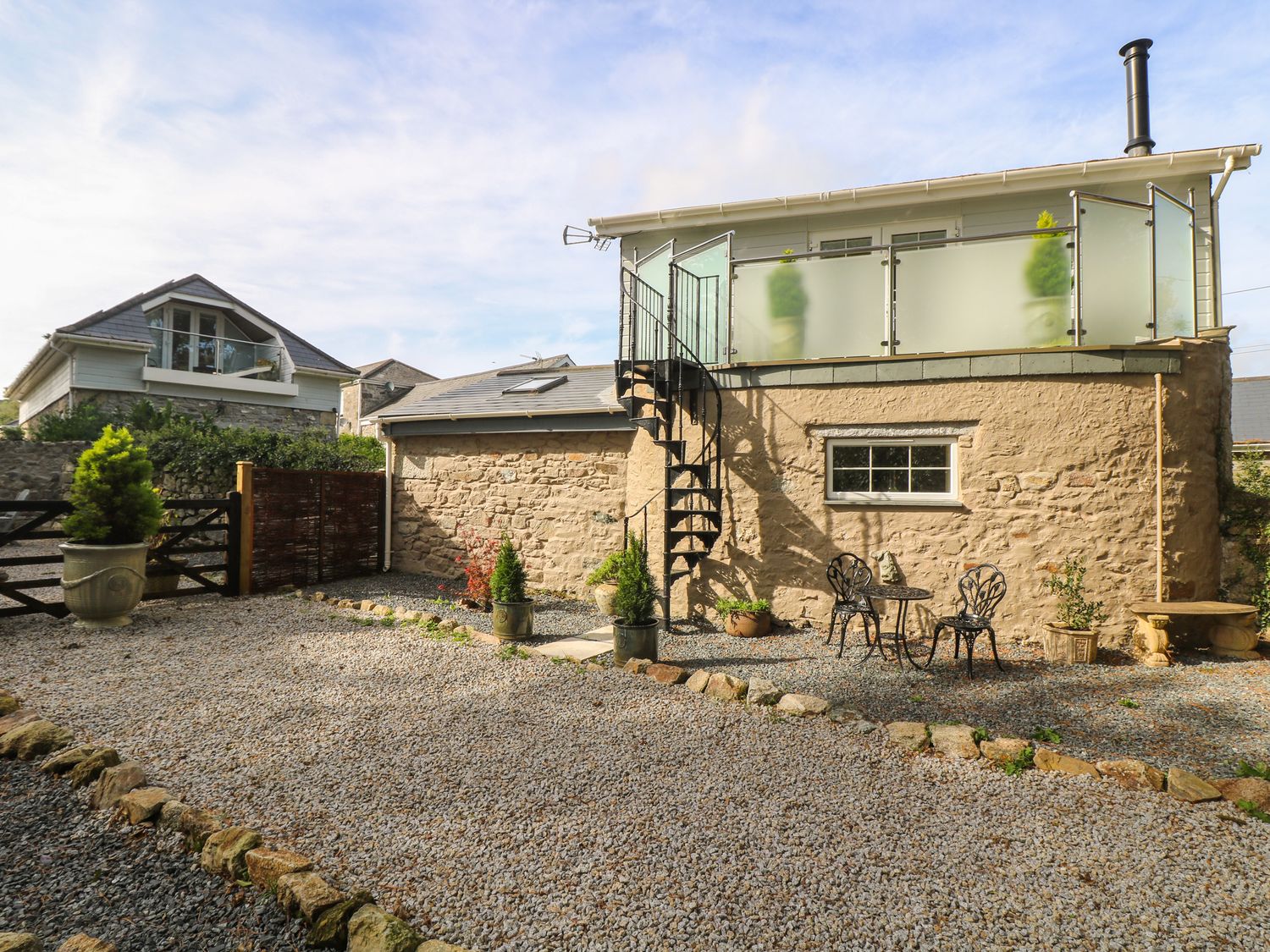 An outdoor patio area with gravel ground two metal chairs and a table a spiral staircase and potted plants at The Old Well House in St Day near Porthtowan