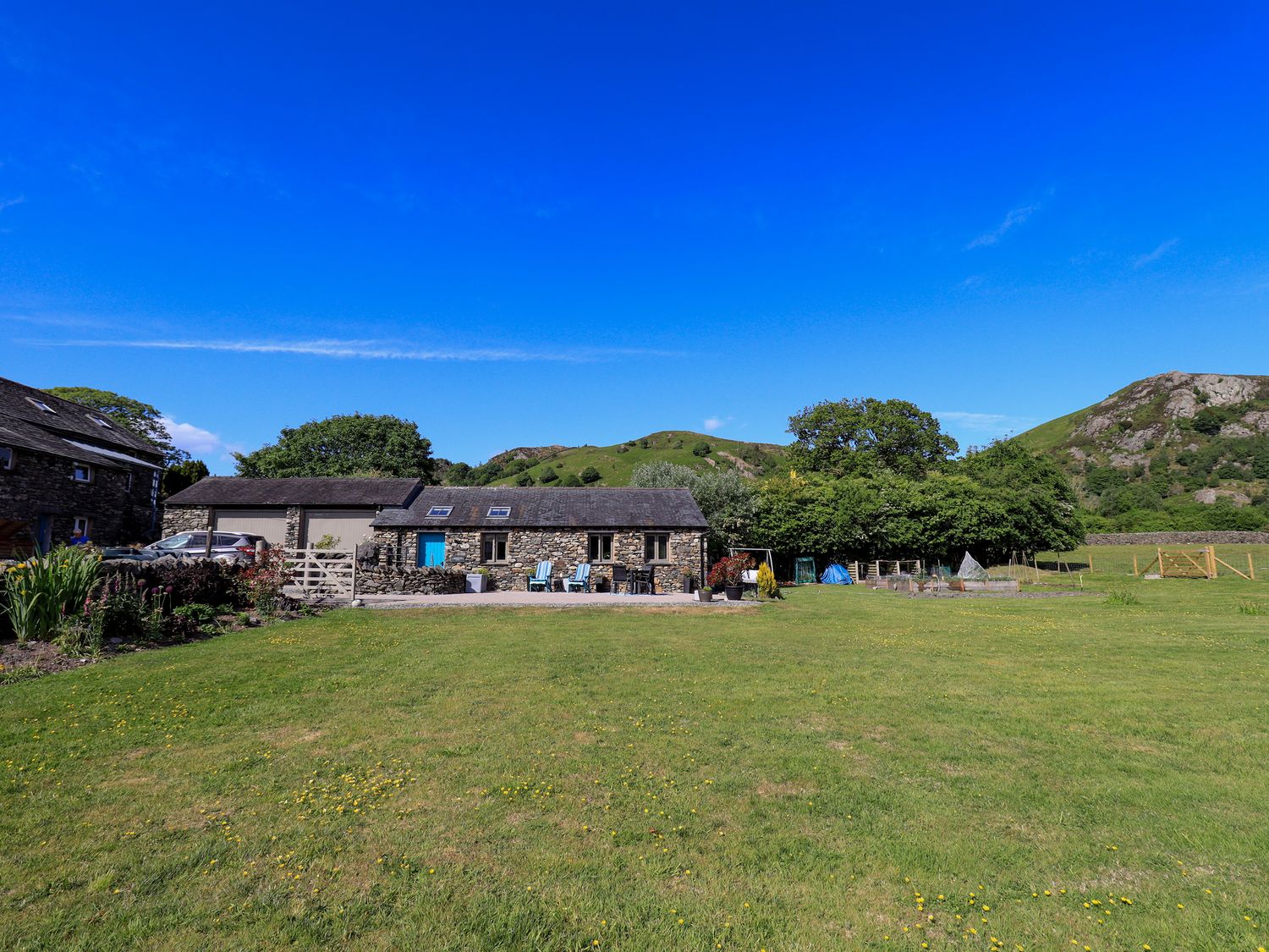 An outdoor area with a stone building and hills in the background at The Garden Suite at Fiddler Hall Barn, Newby Bridge